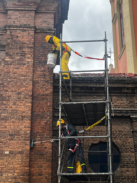 Técnicos de restauración del IDPC sobre andamios realizando labores de limpieza y lavado controlado en la fachada de ladrillo de la Iglesia de Las Cruces.